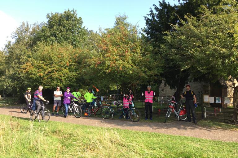 Picture of many cyclists enjoying a break outside a Church.  The heritage cycle tour was part of the Heritage Open Days 2021 an annual September event held nationally.  Milton Keynes has over 100 event every year.