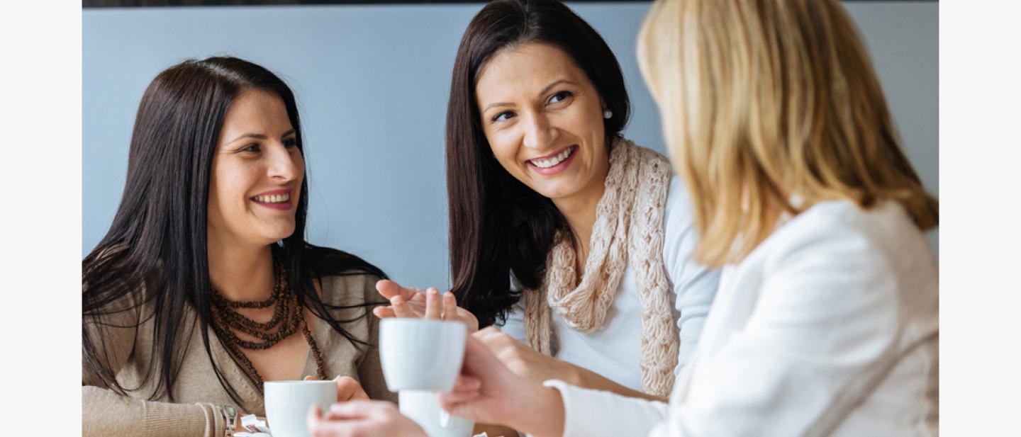 Three women smiling and chatting over coffee.