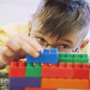 Young boy carefully building a wall with Lego bricks.