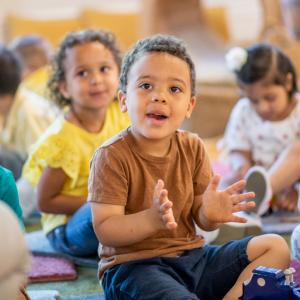 Children sitting on the floor listening to a story and smiling.